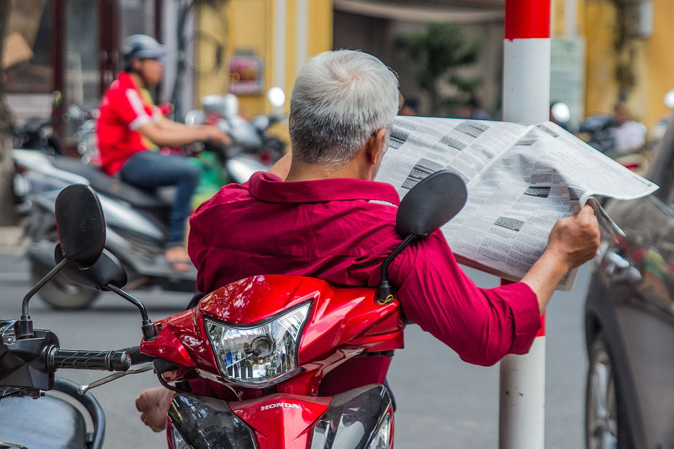 A man sits on a motorbike and read a newspaper. 