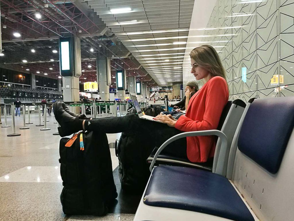 Mulher sentada com o computador na mão esperando no aeroporto de São Paulo porque teve um atraso de voo. 