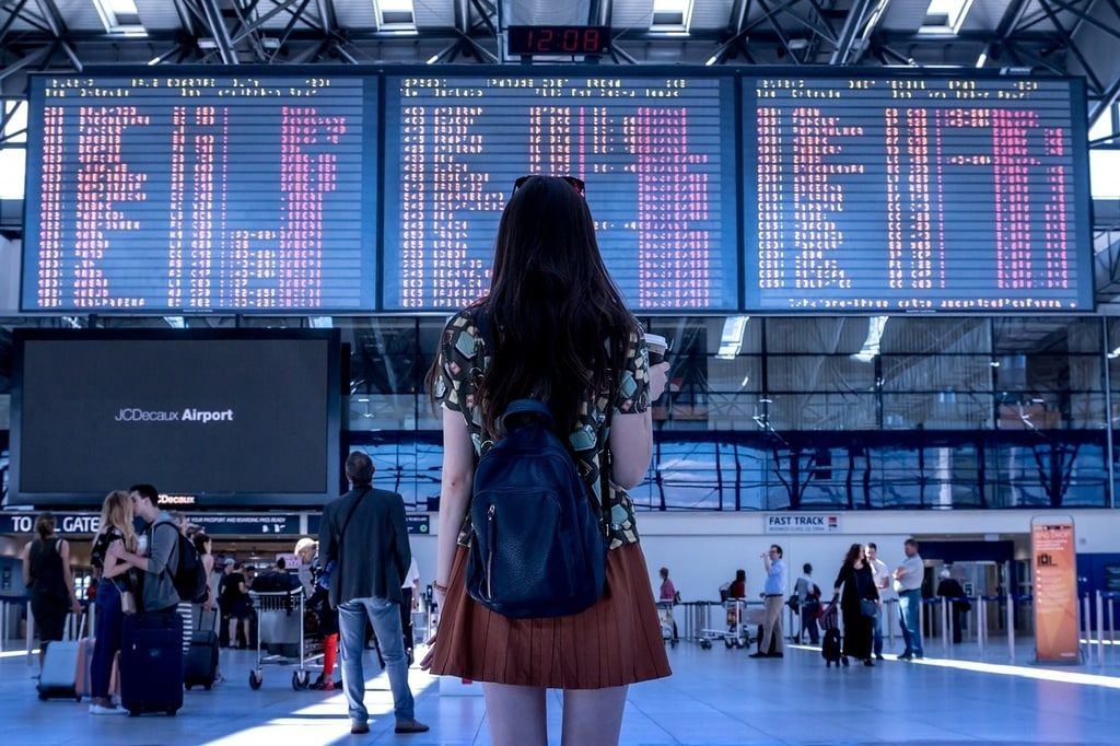 Mulher de pé em um aeroporto internacional olhado o painel com as informações de voo atrasado e cancelado.
