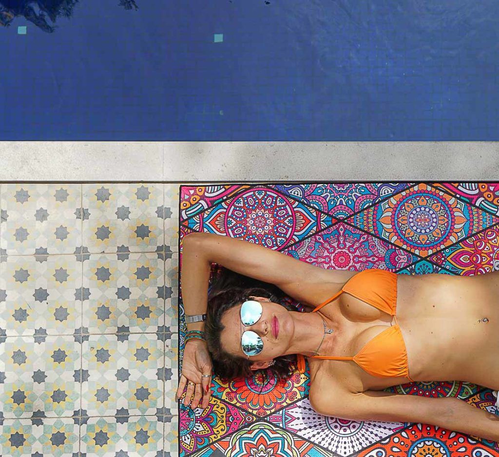 Mulher na piscina sobre uma toalha anti areia sugerida como um dos presentes para viajantes neste post.