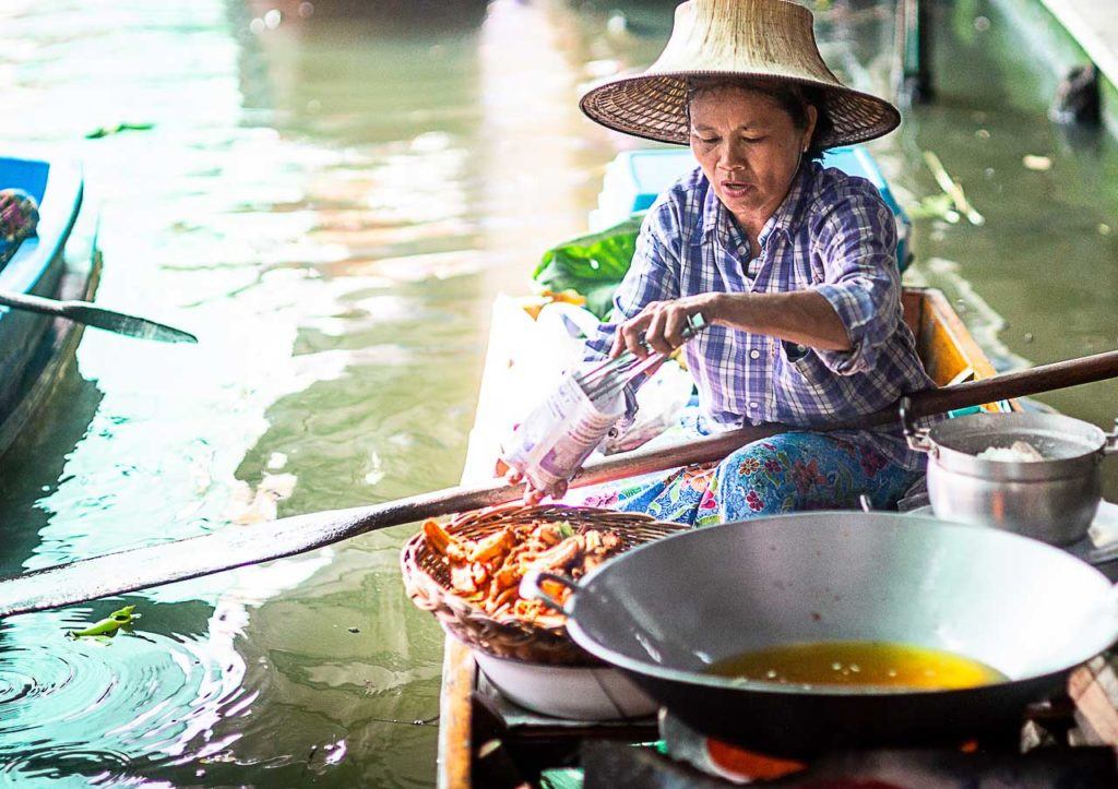 Photo of a floating market in Ayutthaya with a lady cooking on the boat.