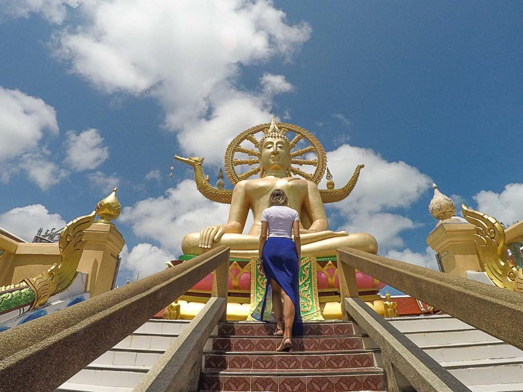 Mulher subindo as escadas de templo tailandês. A Natalie/Nat é a autora deste artigo sobre como viajar para Koh Samui.