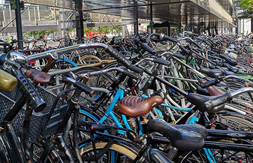 Many bicycles at a parking area. Find here useful tips to plan your Amsterdam trip budget, we covered all trip costs in this post.