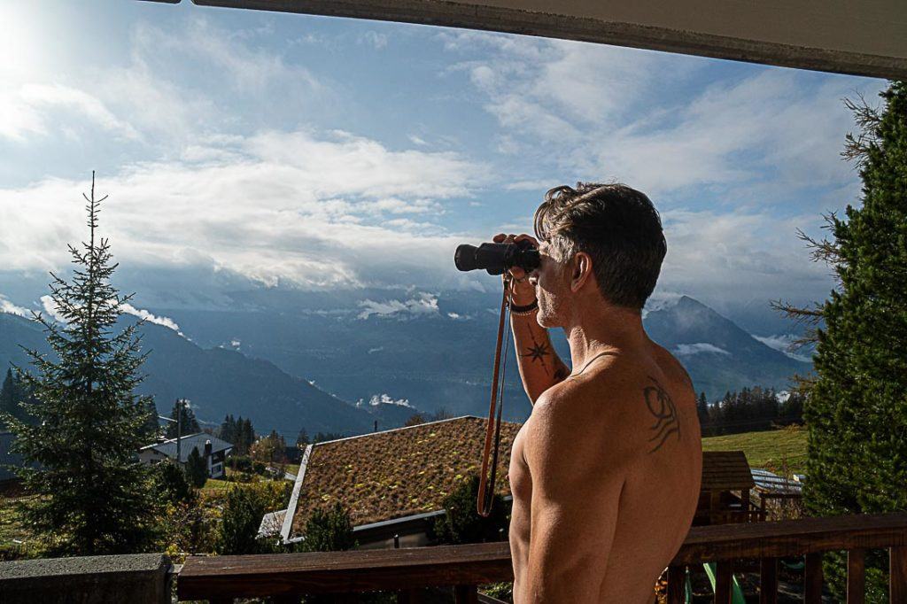 Um homem olhando para o Monte Rigi com binóculos da sacada do seu hotel. 