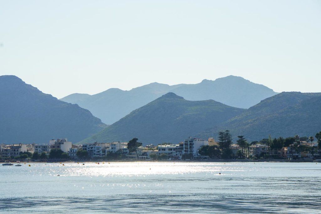 Photo of Puerto Pollensa in Mallorca, where you can see the sea, the town, and the Tramuntana Mountain range in the back. 