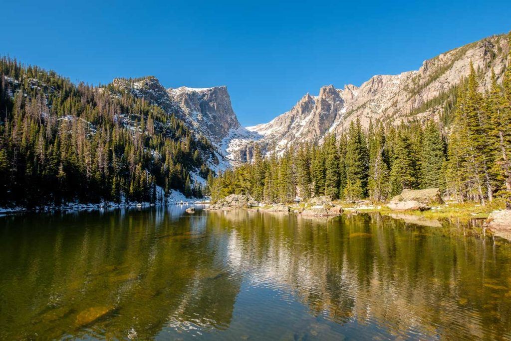Um lago refletindo as montanhas cobertas de neve. Esse é o Rocky Mountain National Park no Colorado, EUA.