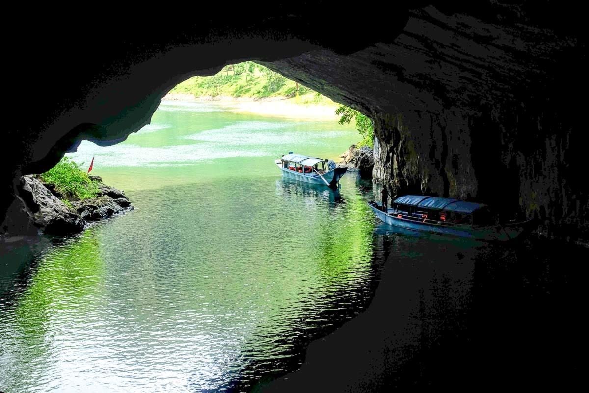 Photo of a cave near a beach with two small boats getting inside the cave. Many people travel to Vietnam to visit the caves. 