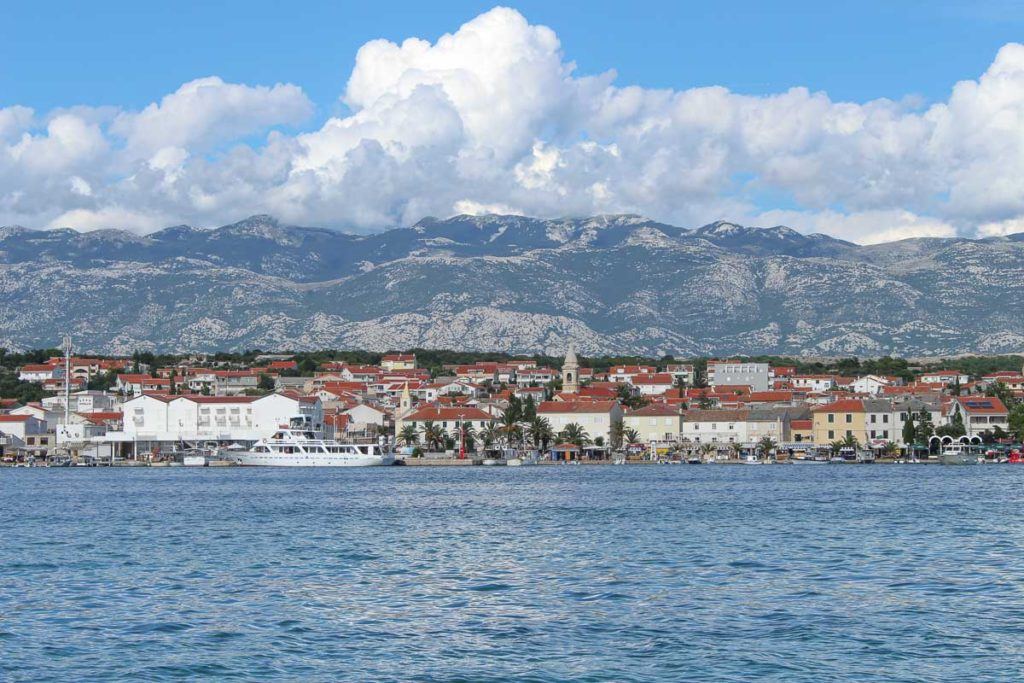 Photo of a town on an island in Croatia. The photo was taken from the boat, you can see the houses in the front and the mountains in the back.