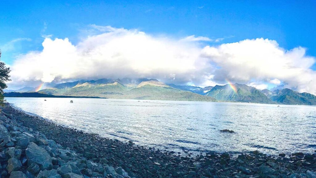The Resurrection Bay is another stop you must add to your road trip to Alaska. It fits perfectly on an Alaska 7 day itinerary. The photo shows the bay and a tiny rainbow forming between the clouds and mountains.