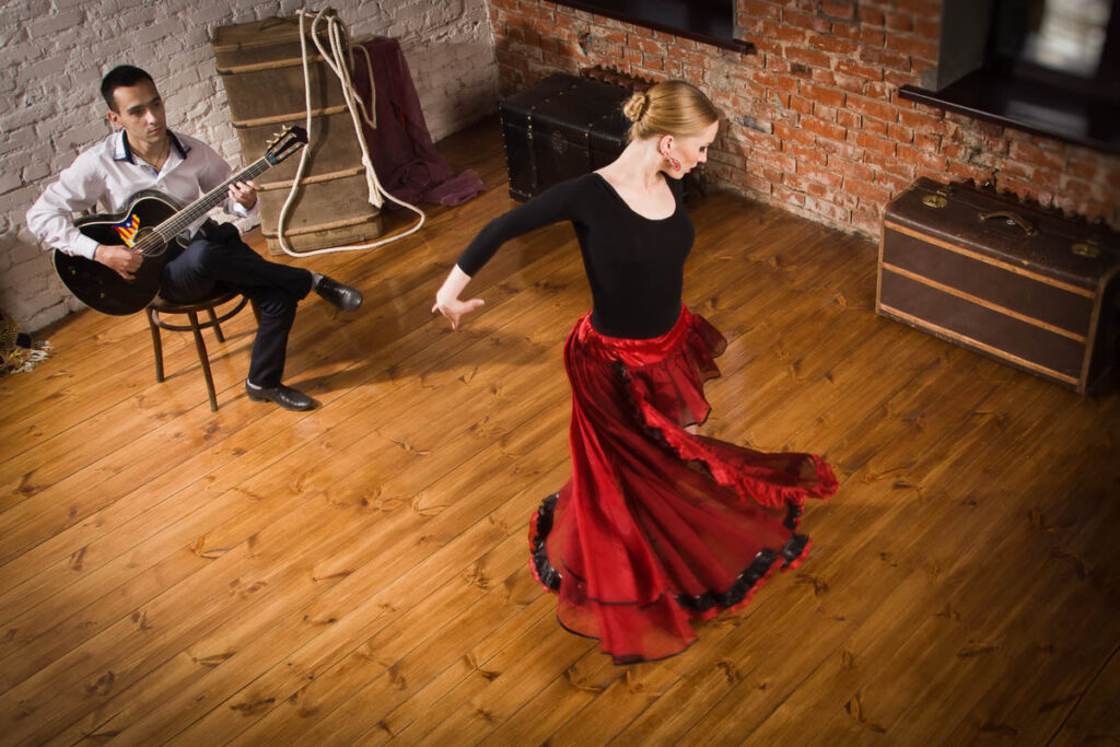 Young woman dancing flamenco in traditional flamenco dress and a man playing the guitar