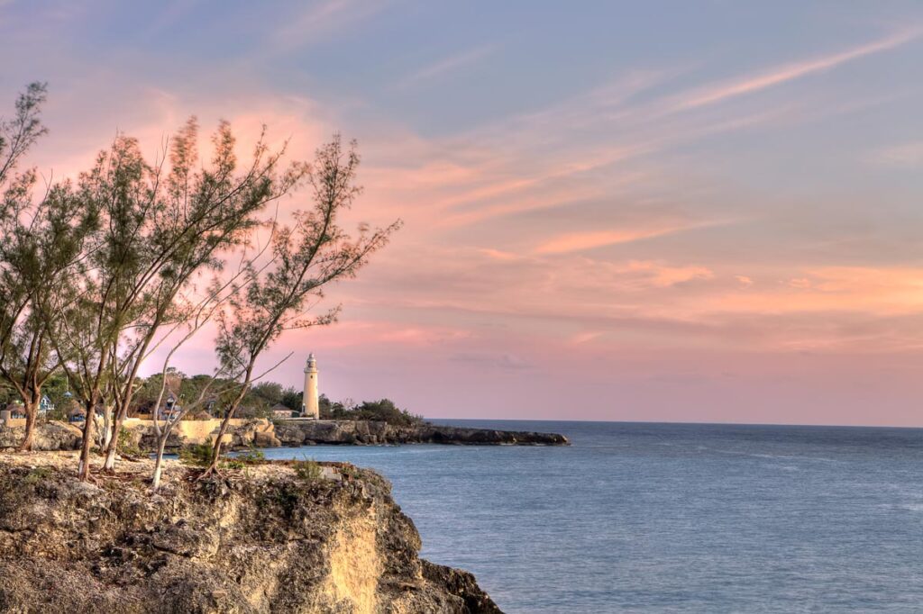 Photo of Jamaica's coast. There is a lighthouse in the background surrounded by cliffs.
