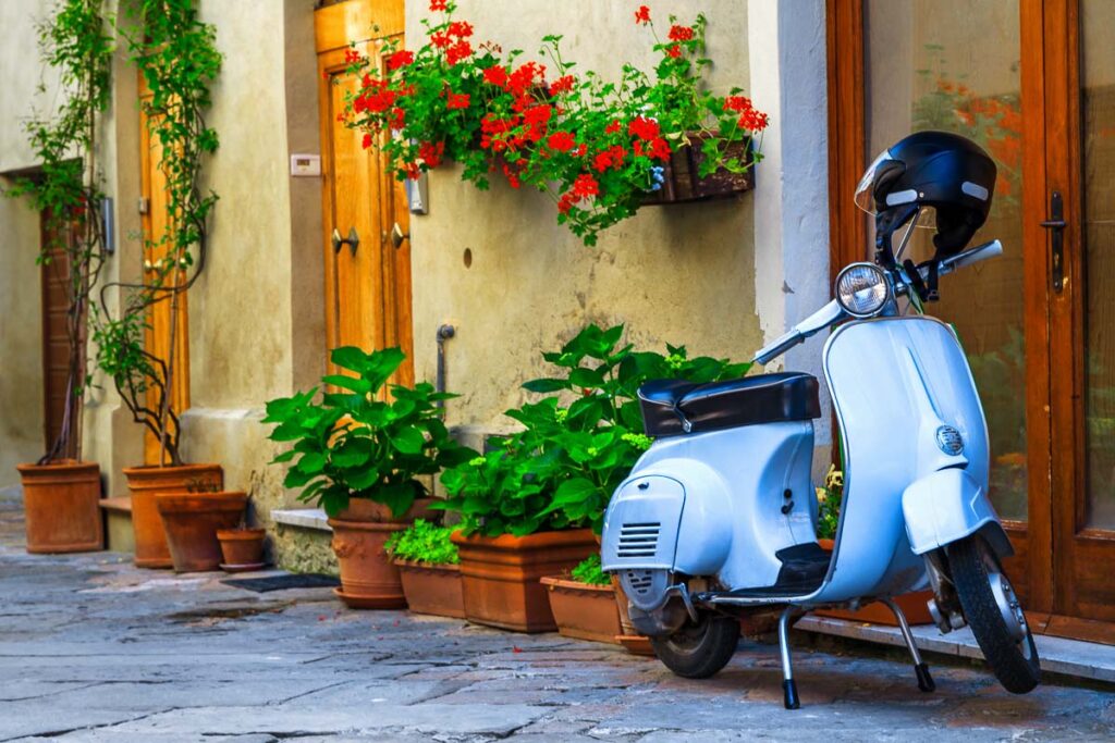 Gorgeous cute decorated street with flowers and rustic entrance, old fashioned scooter standing in typical Italian street, Pienza, Tuscany.
