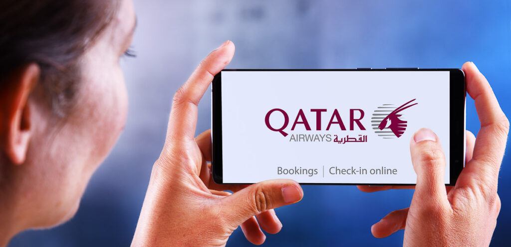 A women holding a mobile phone with  a page of Qatar website on the screen and ready to use the QVerse service.