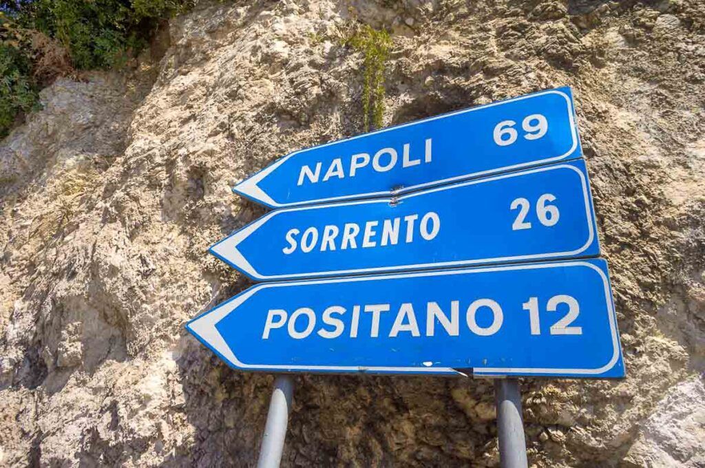 Road signs show how far Napoli, Sorrento, and Positano cities are from each other. Most of the public transportation between the cities will stop at Sorrento.