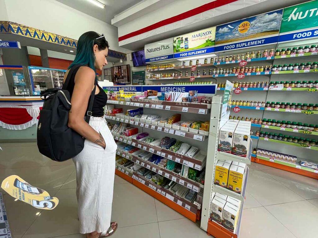 A woman inside a pharmacy in Bali is looking at over-the-counter medication shelves. 