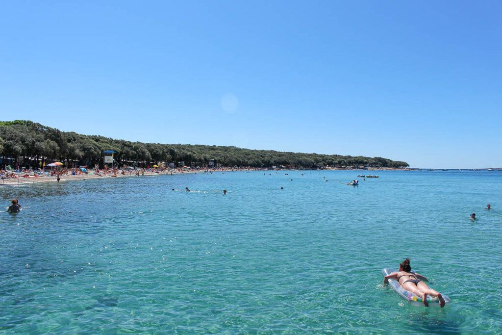 Pag Island is a famous Croatia island, but it still has some secret spots. The photo shows a few people in the crystal clear water and others on the sand relaxing.