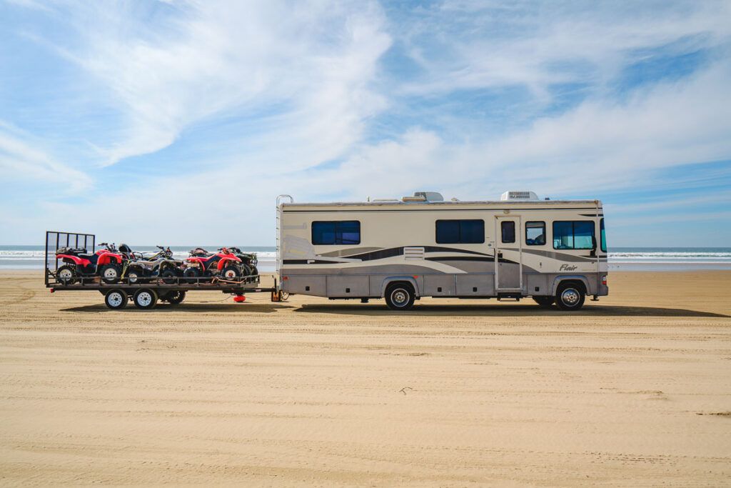 The photo shows the Oceano Dunes State Vehicular Recreation Area with an RV vehicle pulling a couple of ATVs. This is the best place to go for ATV riding in Pismo Beach. 
