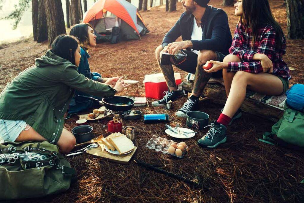 People are cooking at a camping site. It looks like friends sharing a special moment while traveling on a budget.