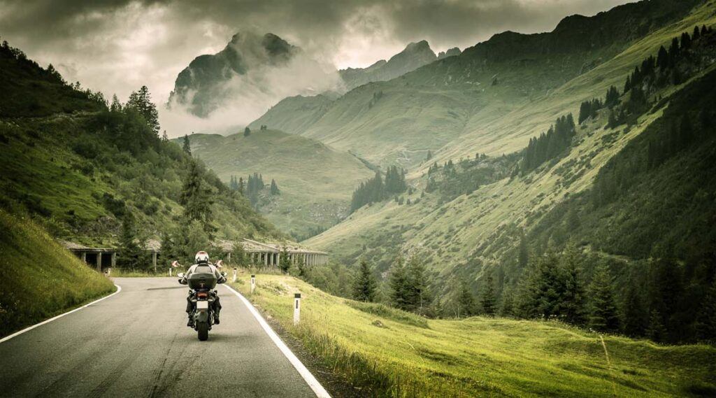 Motorcyclist on a mountainous highway, cold overcast weather, looks like he is on a cross-country motorcycle trip in Europe. 