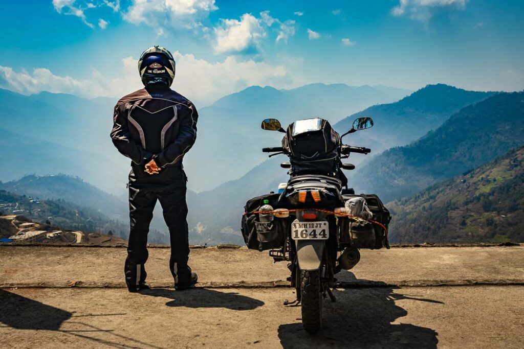 A motorcyclist with his loaded motorcycle and pristine natural view in the morning. It looks like here is taking a break from his motorbike cross-country trip.