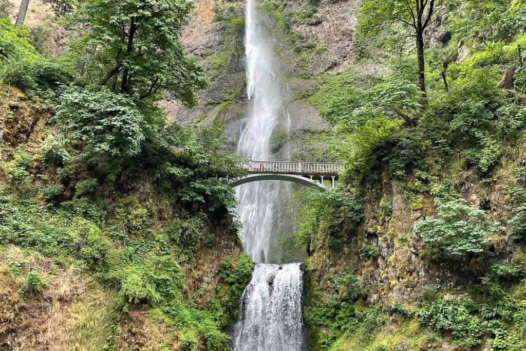 A photo of Columbia River Gorge with its incredible waterfall and a bridge cross on top of it. It's a must-visit place in Oregon. It's the perfect day trip from Portland. 