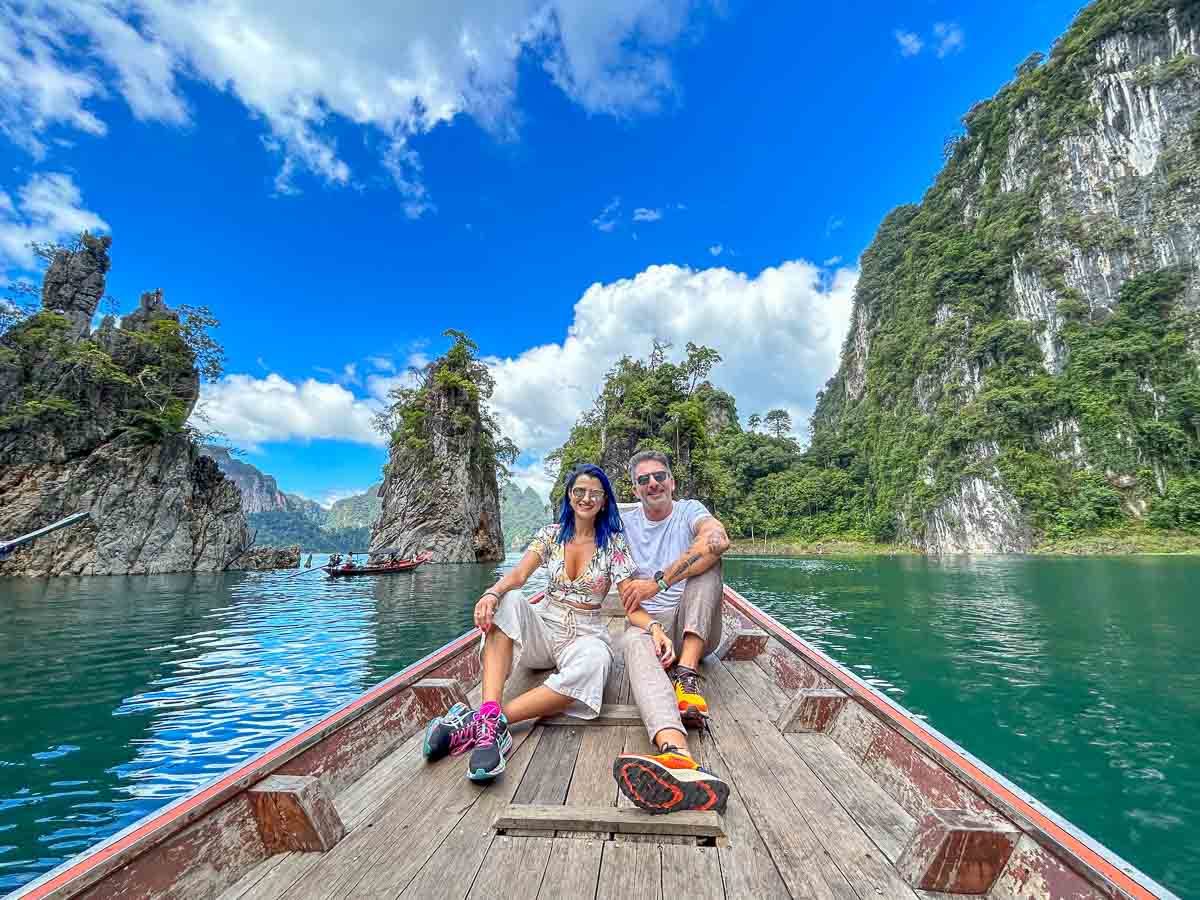 Photo of a couple on a longtail boat in Khao Sok Park taking a picture in front of the Three-brother Pillar, an ionic rock formation at the National Park.