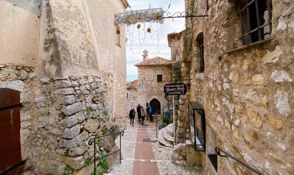 Medieval cobblestone streets of Èze Village on the French Riviera. It shows the old houses and some tourists walking between them. 