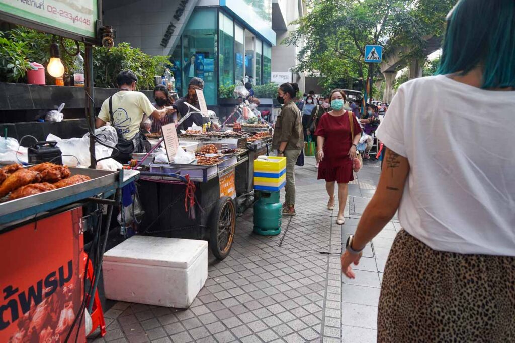 Bangkok é segura para mulheres que viajam sozinhas. Esta foto mostra Nat andando pela área de Silom em Bangkok com muitas pessoas ao redor e vendedores de comida de rua.
