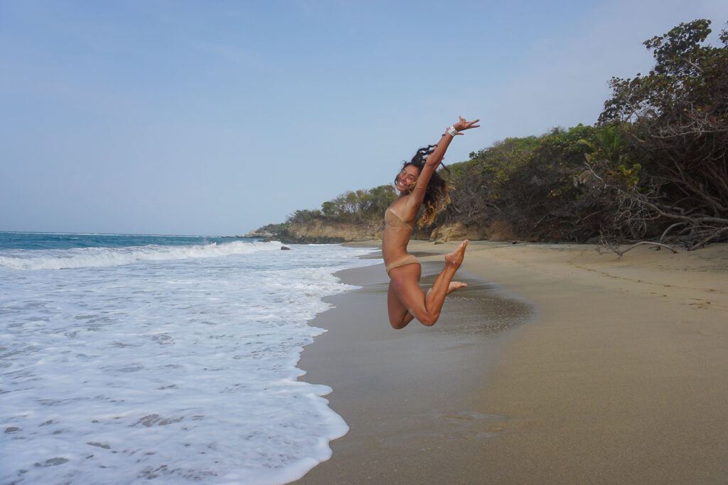 Woman jumping on the sand of a beach in Tayrona National Park in Colombia. 