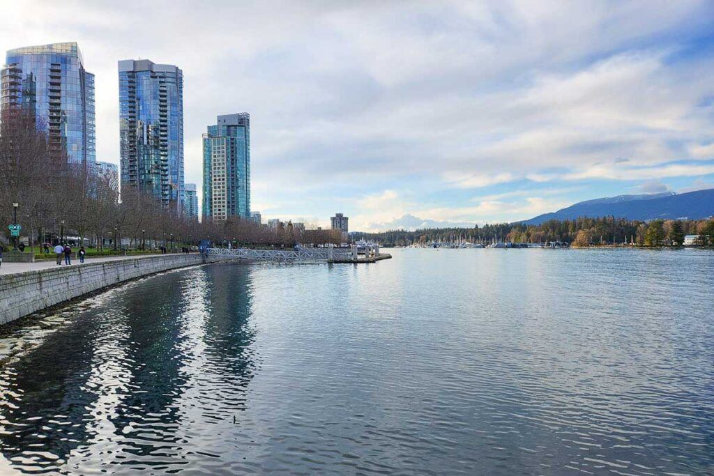 Coal Harbour photo showing the water, the waterfront walkway, modern buildings on one side, and Vancouver mountains on the other.