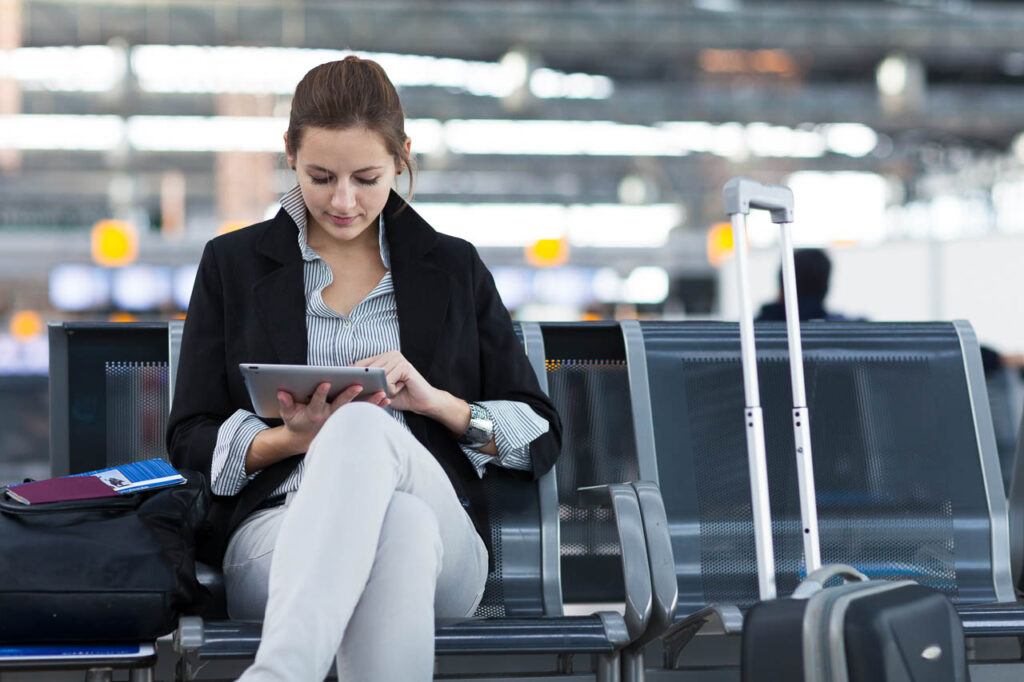Young passenger at an international airport, using an Ipad while waiting for her flight.