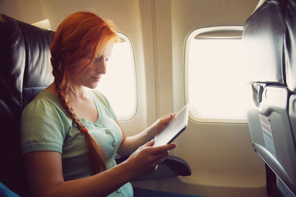 Woman using a tablet on a plane. It's the best way to enjoy the flight. You can watch movies or read on your travel tablet. 