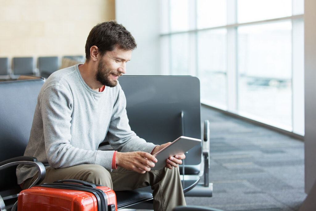A smiling man using a tablet in the airport while waiting for his international connection. 