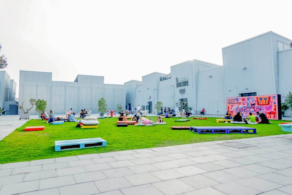 A view of locals and tourists sitting on top of a lush green field in Alserkal Avenue in Dubai, UAE.