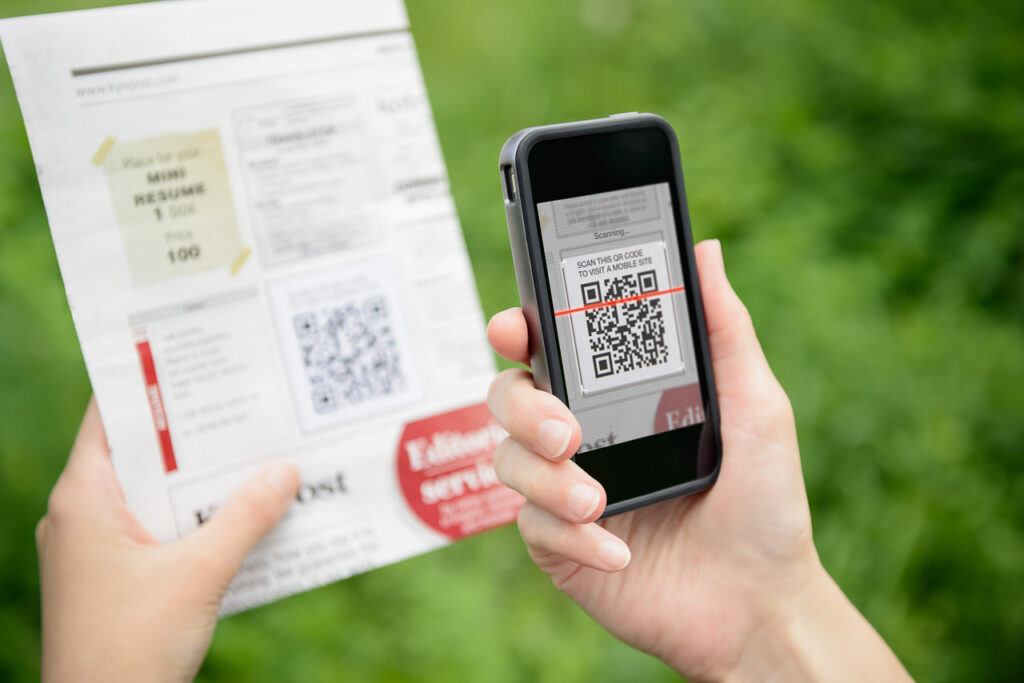 A person holding a cell phone and scanning a flyer with touristic information about an attraction. It is another common way QR code for travel is used.