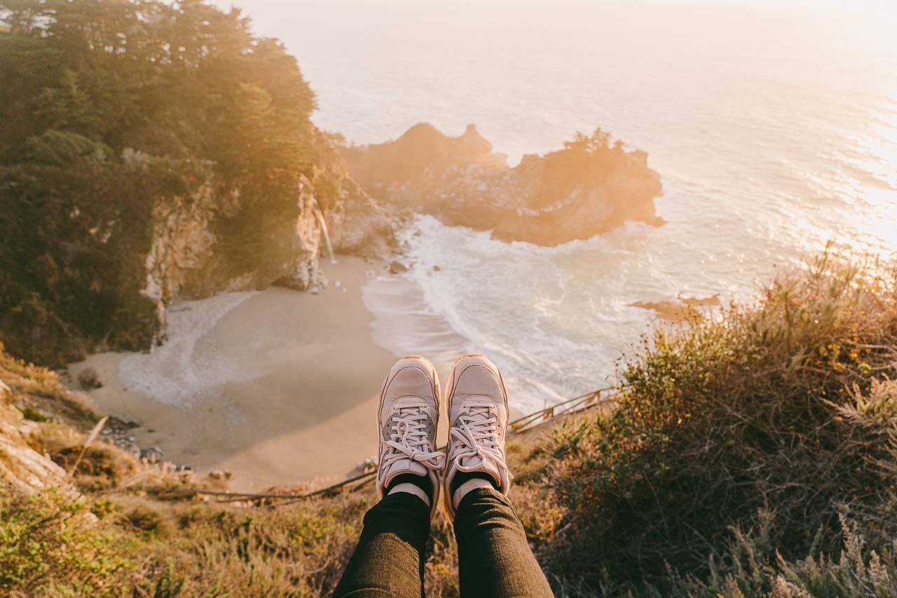 Woman sitting on the edge of a cliff facing a small secluded beach. It shows one of the spots you can visit on a weekend getaway in Northern California, US.