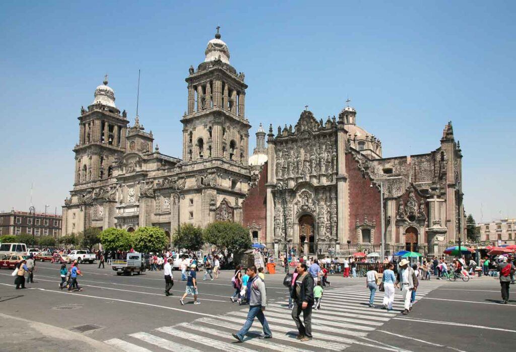 People crossing the street on Plaza de la Constitución or Zocalo in Mexico City on Saturday in front of Catedral Metropolitana, one of the places to visit in Mexico City.