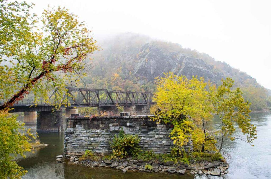 Photo taken at Harpers Ferry National Historical Park. An old bridge, the river, and a hill in the background.