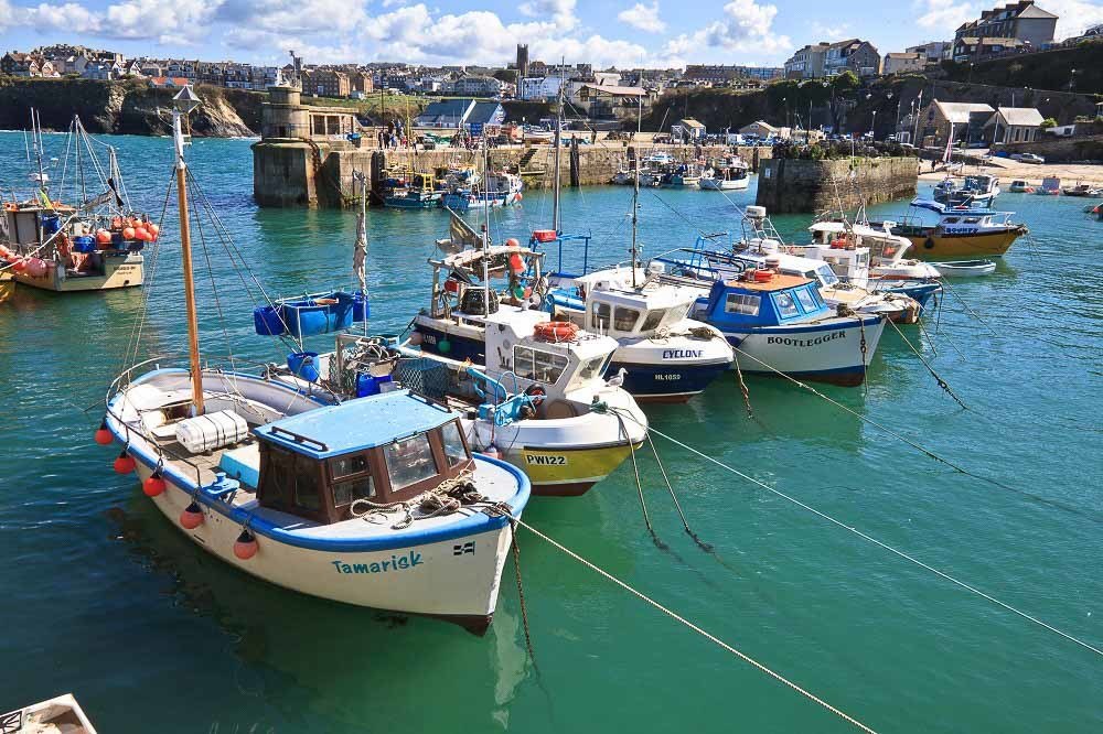 Newquay Harbour by Visit Newquay. The pier with small fishing boats and the town in the background.