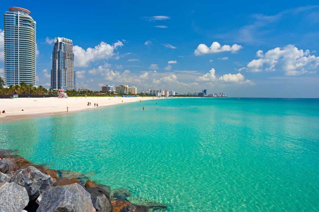 South Beach, Miami, Florida, USA. The photo shows the turquoise water and white sand beach in front and skyscrapers in the background.