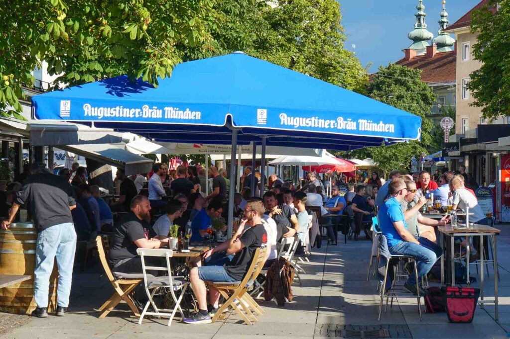 Photo of people enjoying a Saturday morning at LendPlatz square. Lotos of tables and chairs spread over the square and people drinking and eating locally produced food. 