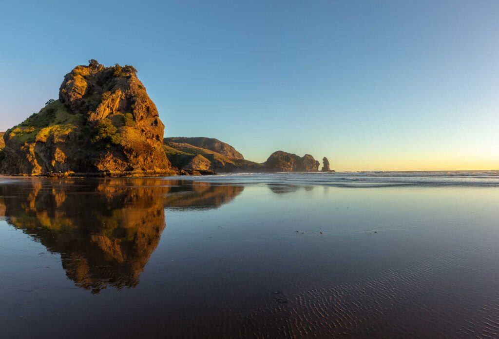 Sunset at Piha beach, North island, New Zealand. On Piha Beach is one of the romantic places to visit in Auckland.