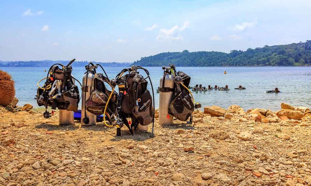 Photo of a beach in Havelock Islands with diving equipment on the sand and people learning how to scuba dive in the water. 