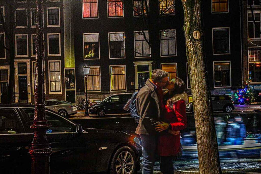 Photo of a couple kissing in front of historical houses in Amsterdam. It happened during the Amsterdam Light festival.