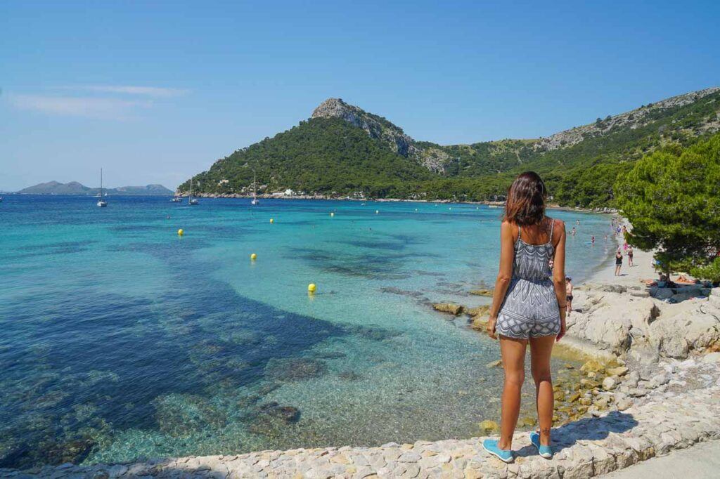 A woman standing on a rock overlooking a beach in Mallorca, Spain.