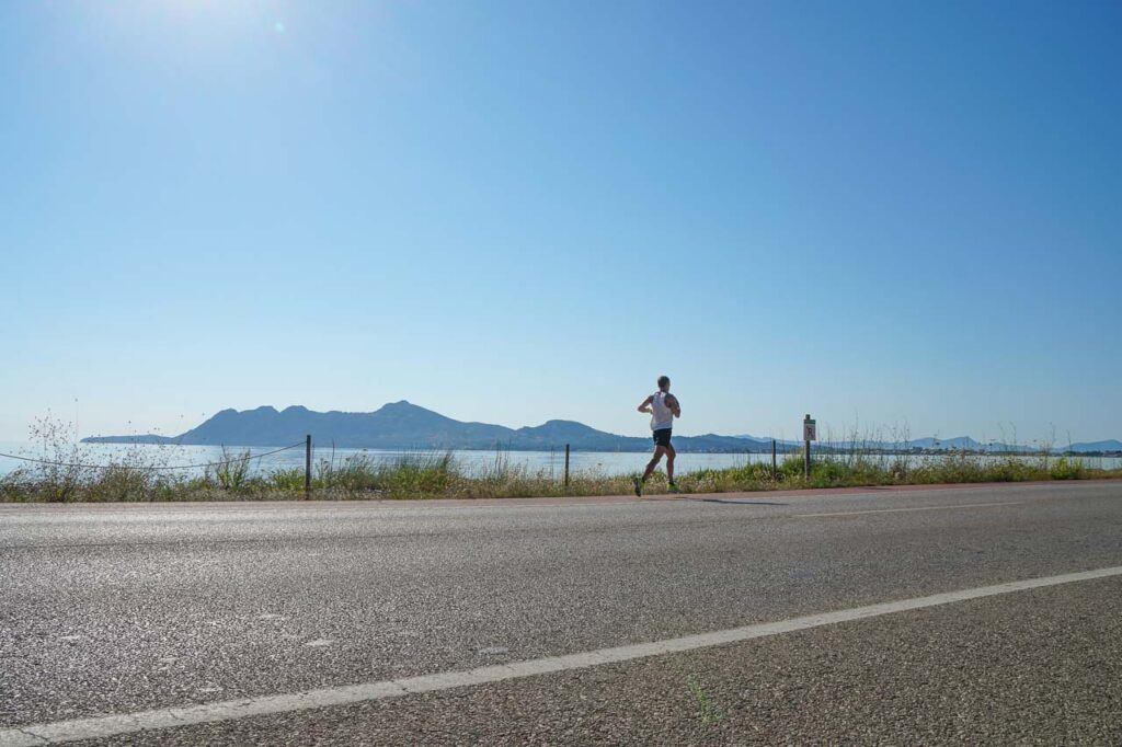 A man running on a road with the bay of Alcudia on the backdrop.
