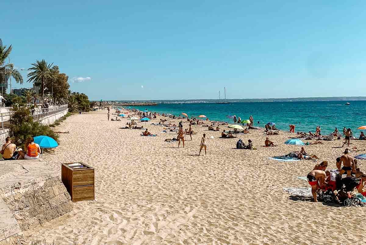 Mallorca sandy beach with people relaxing by the sea. The water is crystal clear.
