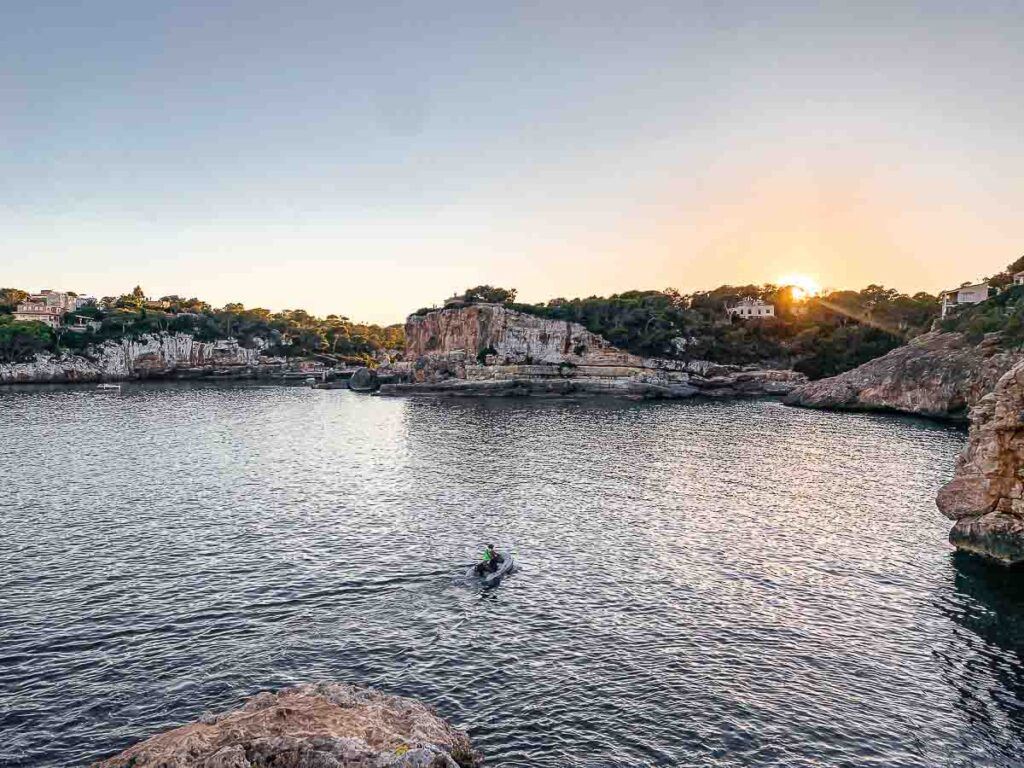 Sunset on the Mallorca Island in Spain. The sun is setting behind the rocks and a tiny boat on the sea.